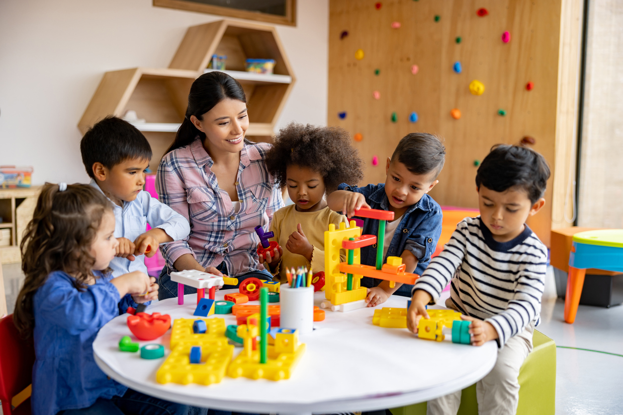 Happy Latin American teacher with a group of elementary students playing with toy blocks